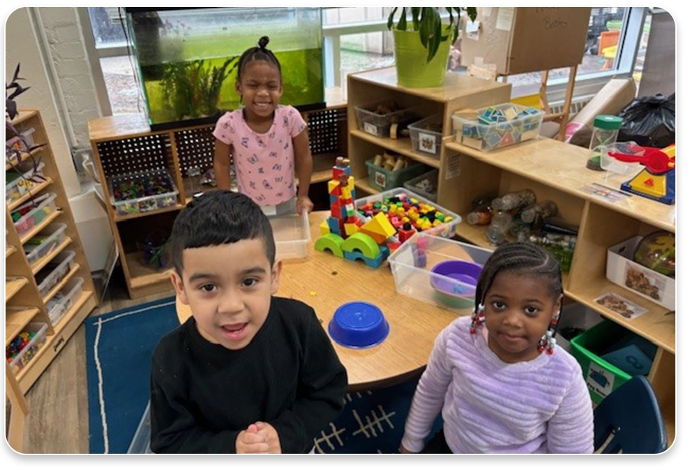 Three children sitting at a table in a classroom.