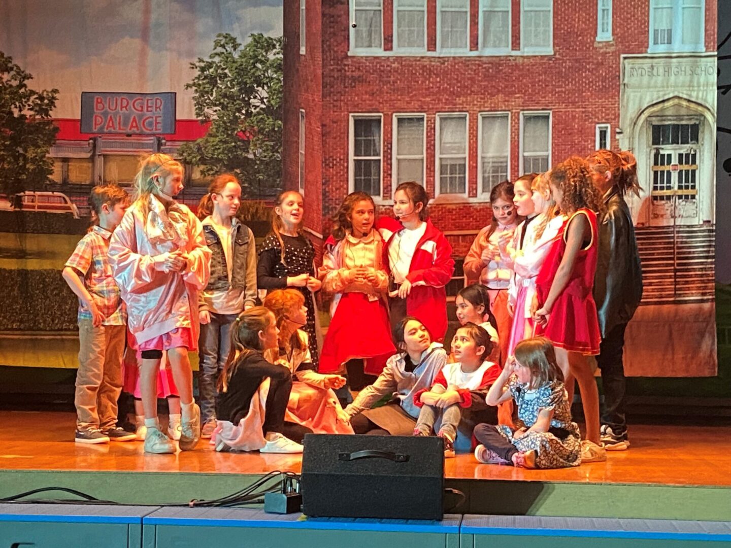A group of children on stage in front of a building.